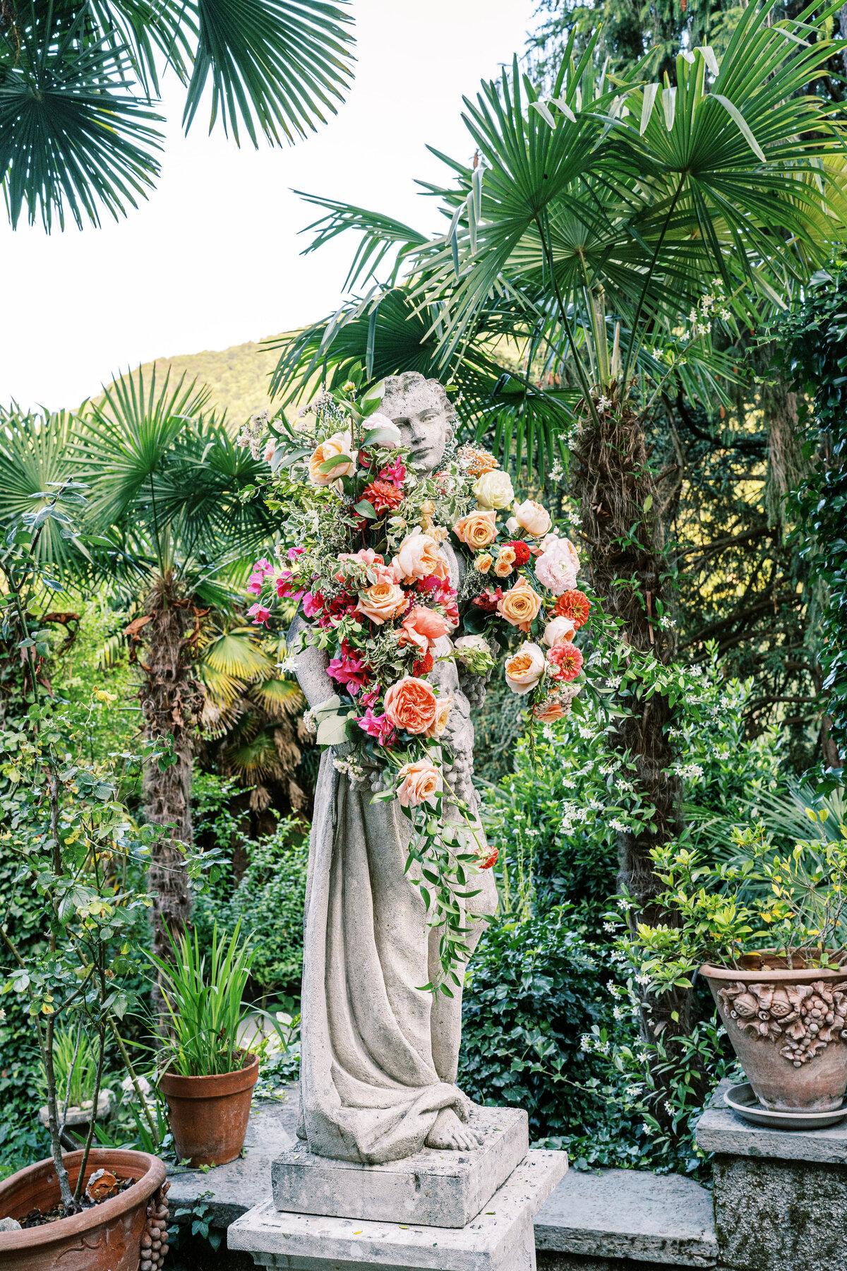 Statue draped in rich colored peonies and garden roses at a private villa wedding on Lake Como Italy photographed by Lake Como Wedding photographer