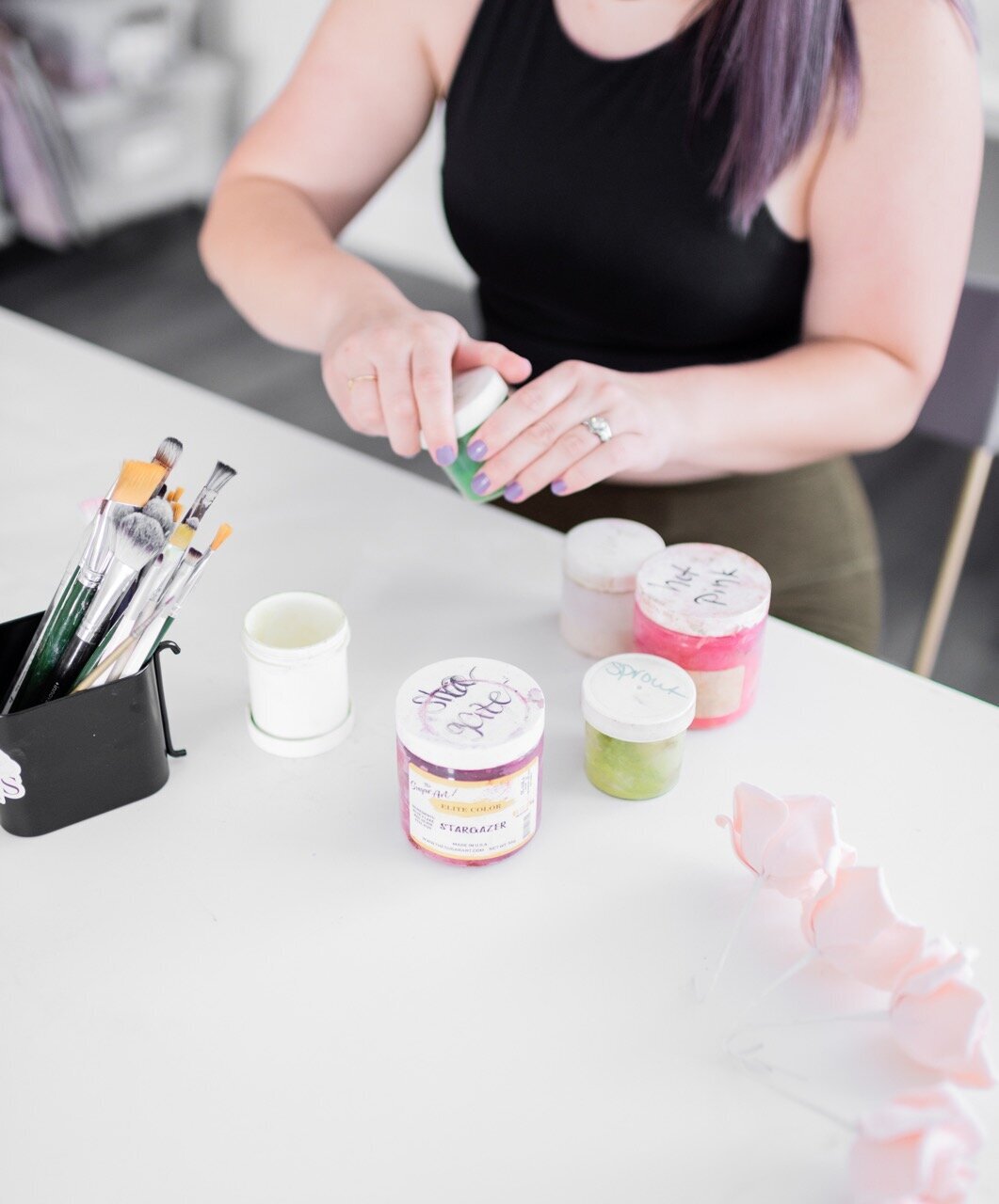Powdered food coloring and paint brushes next to a a woman making blush gumpaste roses