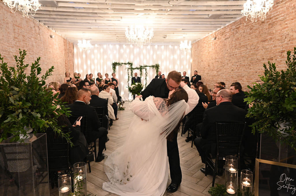 A groom dipping a bride and kissing her in front of guests.