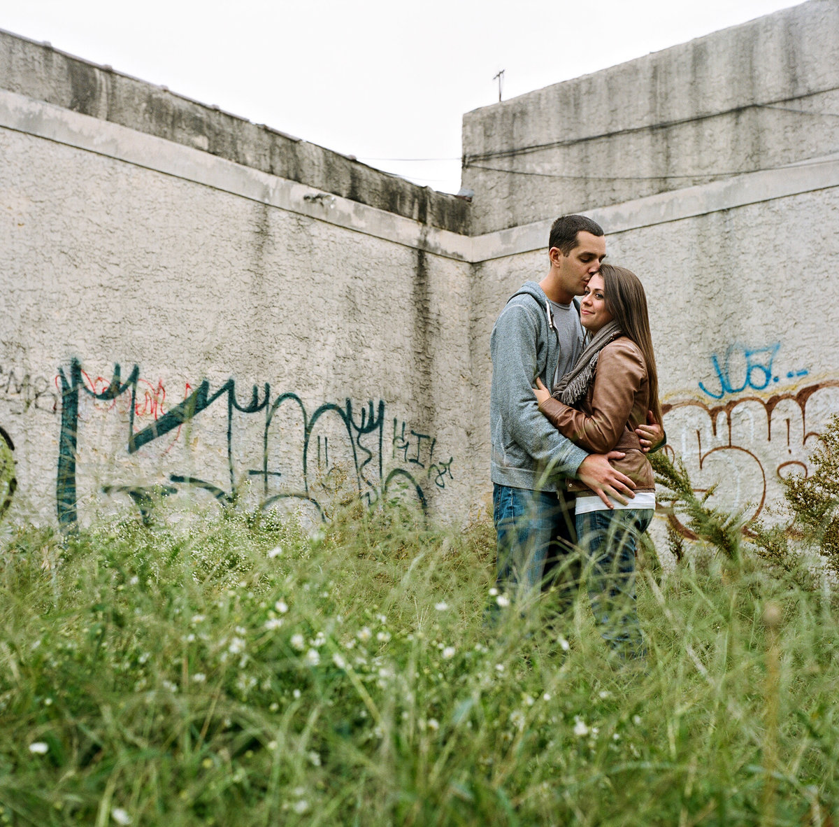 A couple stands in the tall grass in a vacant lot in philly.