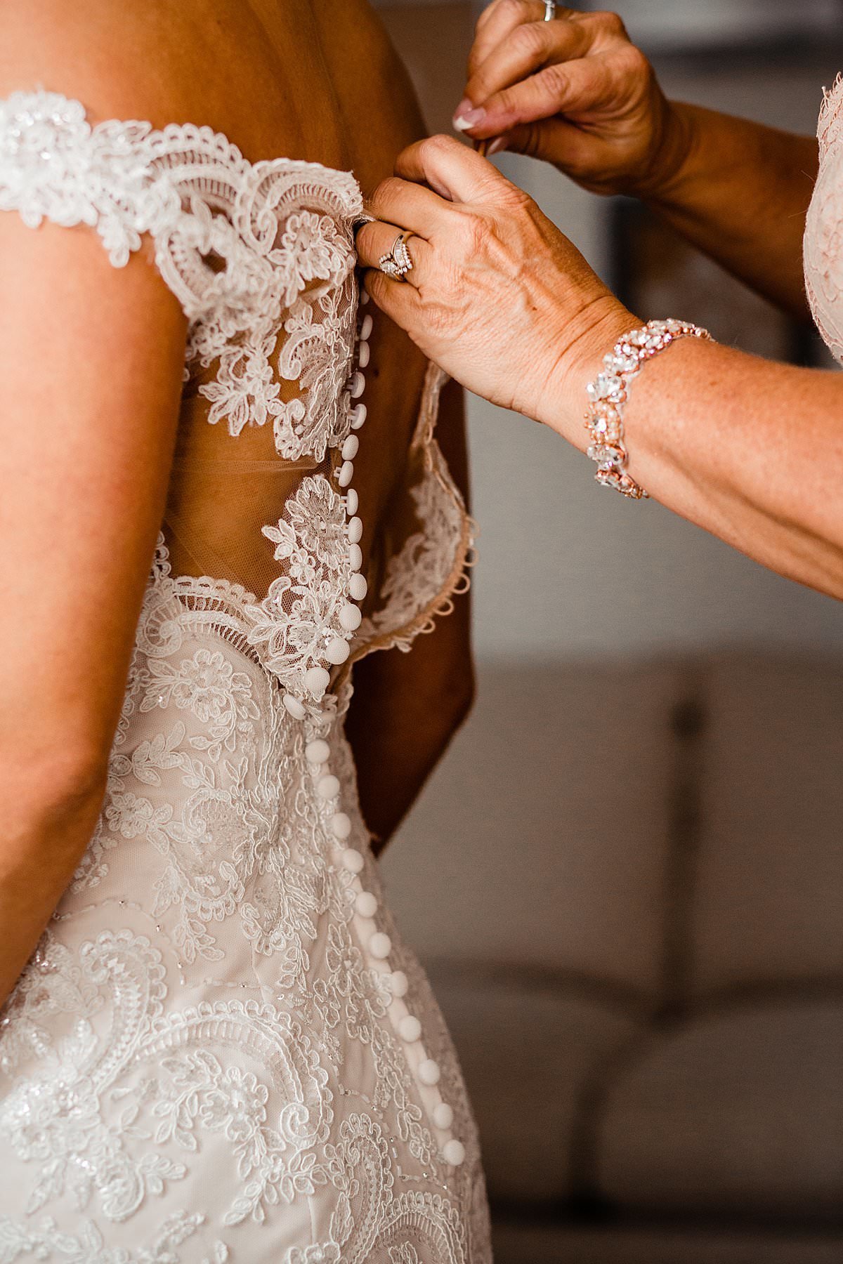 Close up photo of mom buttoning her daughters wedding dress