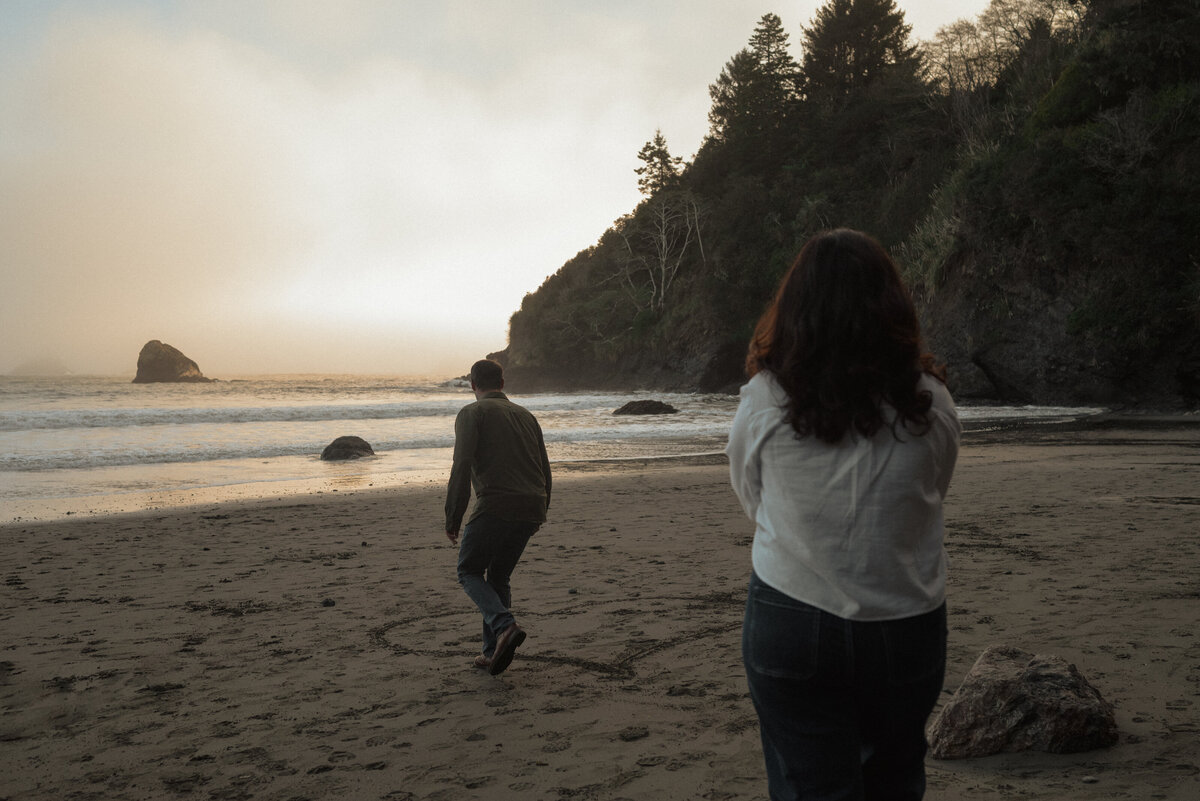 playful engagement moment with couple walking near the ocean waves at sunset