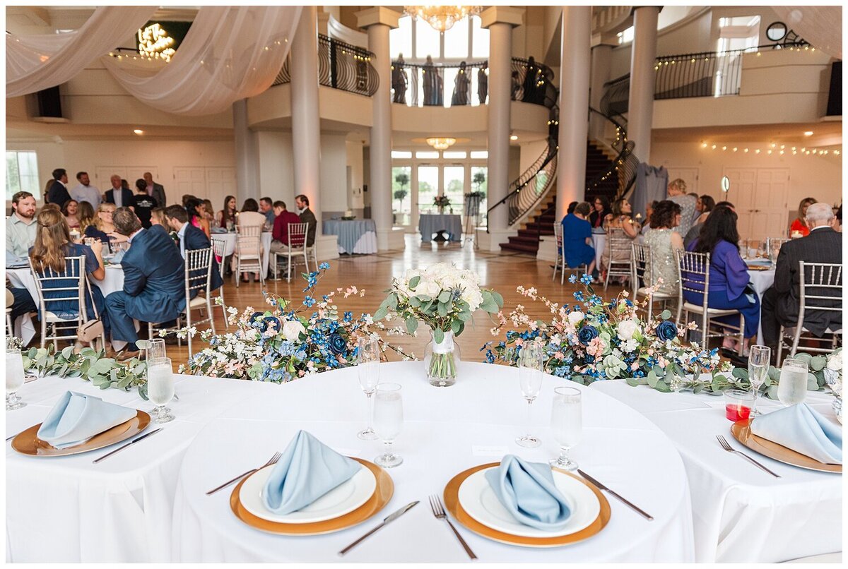 Place setting with gold chargers, white plate and dusty blue napkins with silverware and
