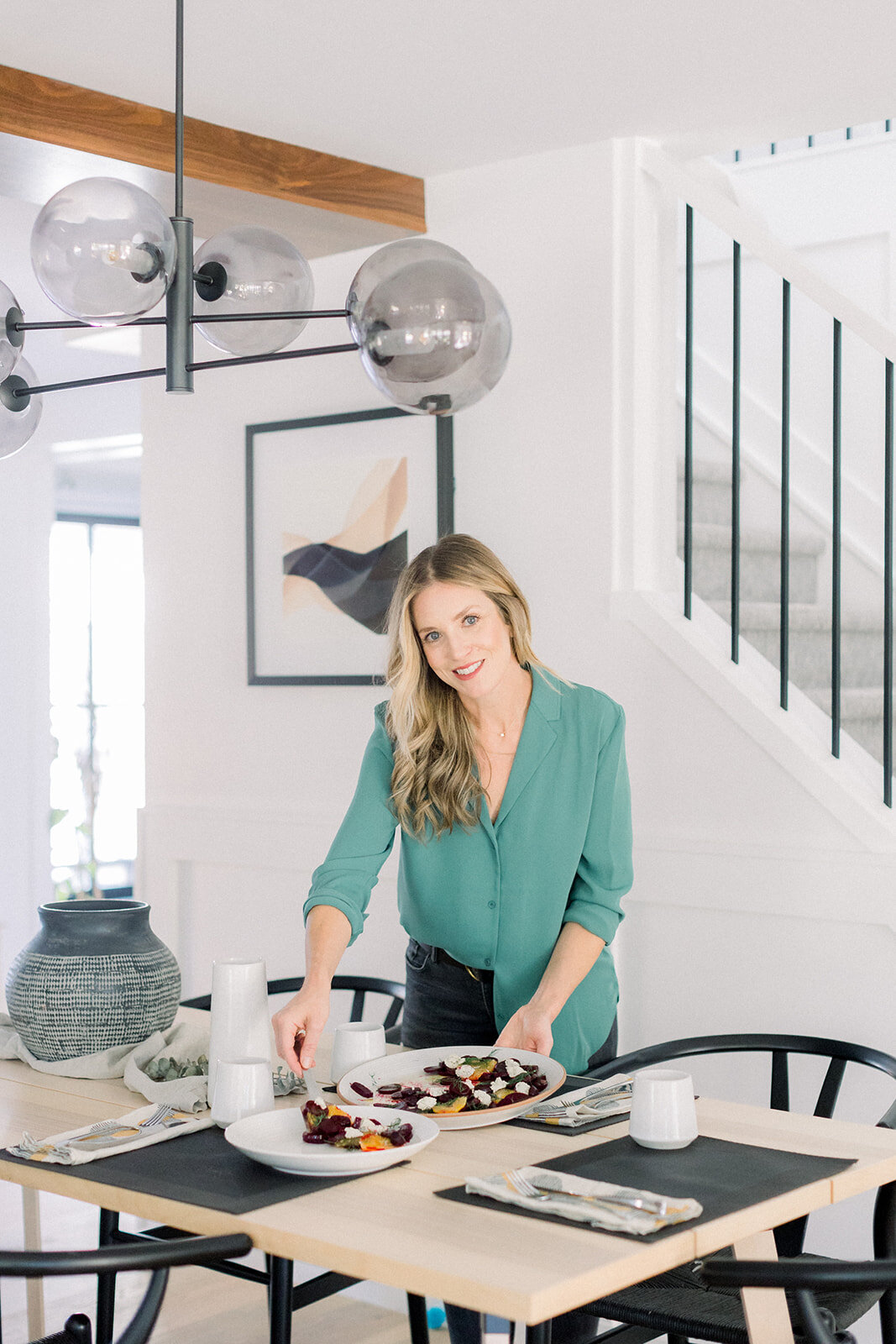 Blonde woman placing plate of food on a table in a bright and airy room