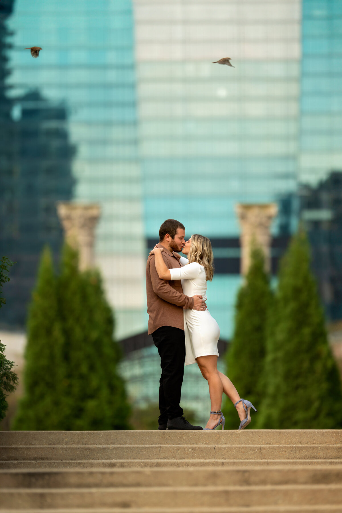 young couple kissing at beautiful cancer survivors' garden in  Chicago while two birds flying above