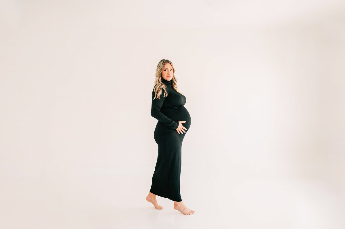 pregnant mom in black dress walking in studio during Springfield MO maternity photography session