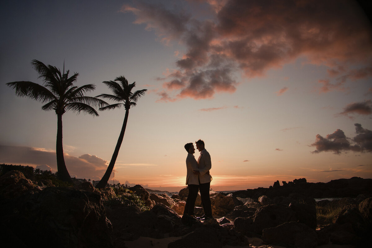 Two grooms standing on rocks at sunset.