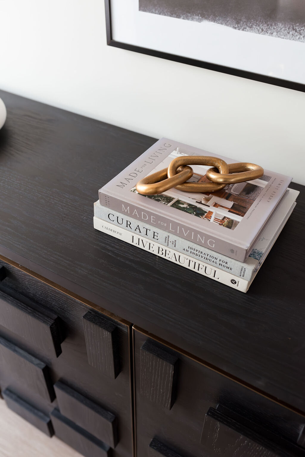 Close up view atop a black sideboard, with neutral books and gold decor on top.