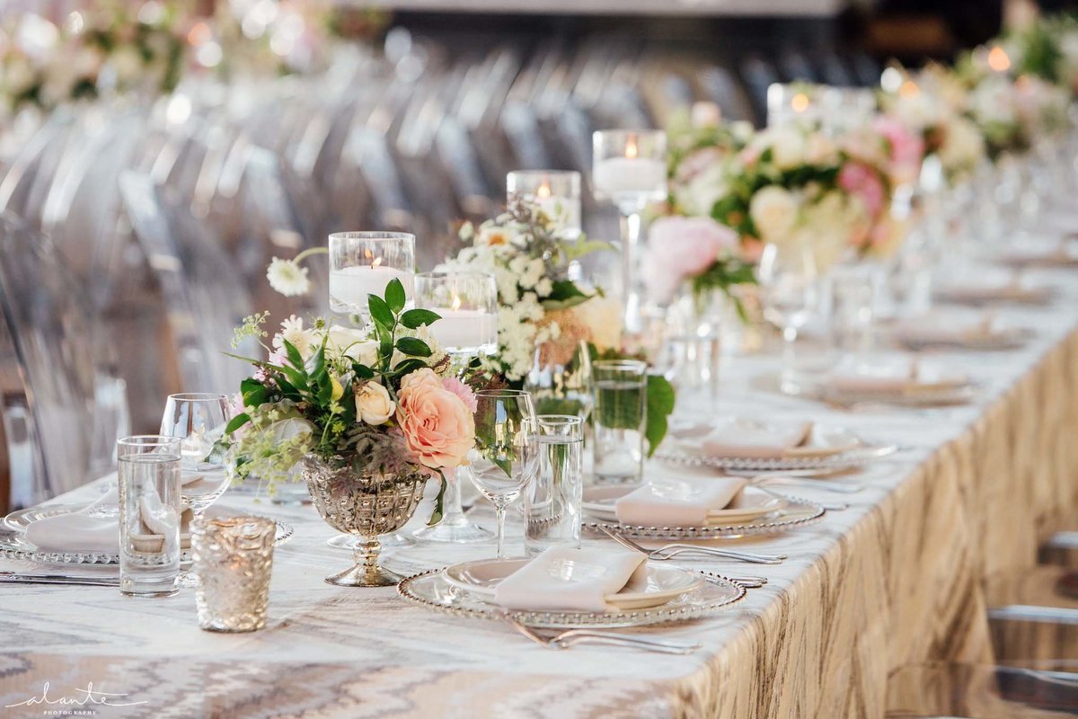 Long wedding reception  tables lined with small blush arrangements  in silver compotes