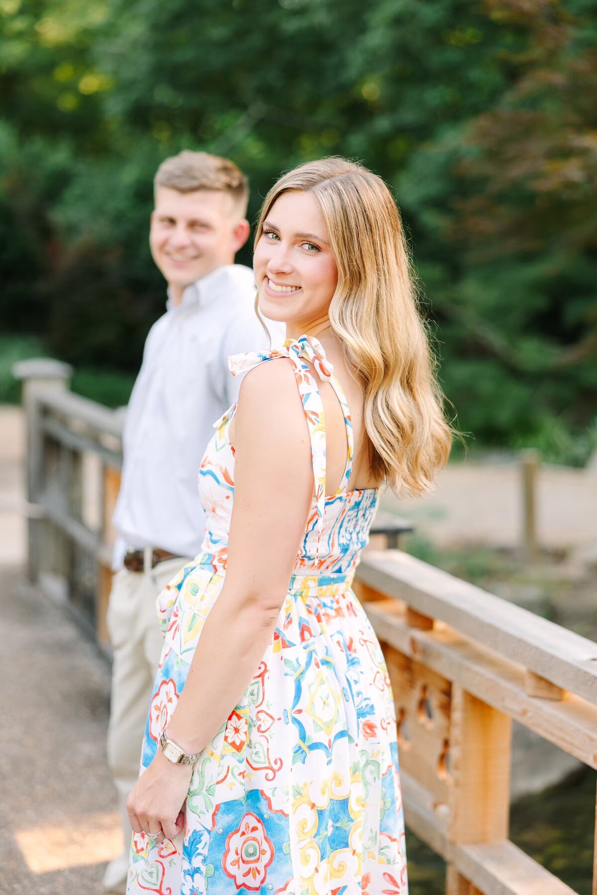 Bride smiles during engagement session as groom looks on
