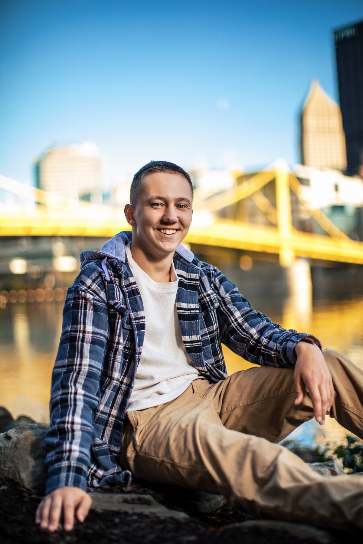 a photo of a young man entering his senior year in high school at Avonworth poses near the famous yellow Pittsburgh Bridge