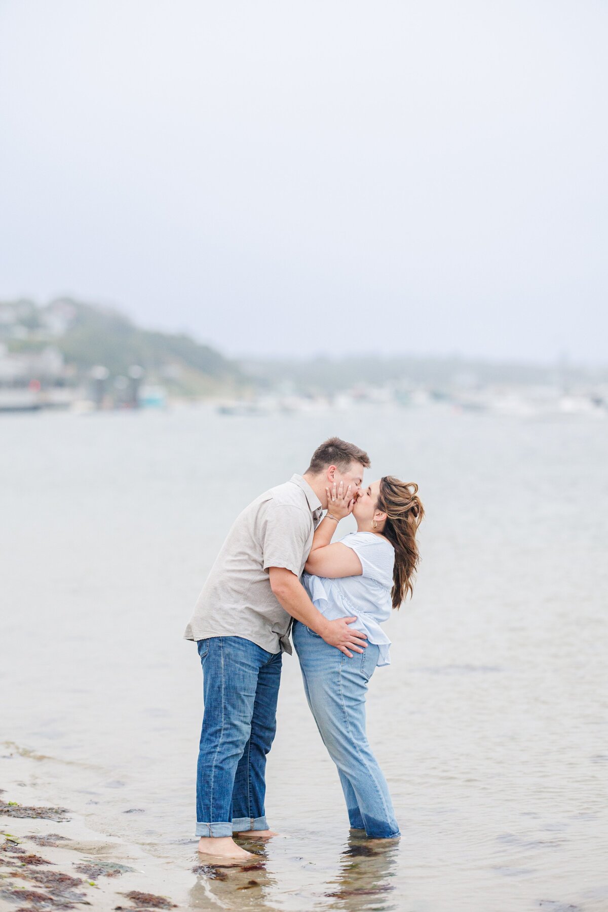 Couple standing barefoot in shallow water, leaning in for a kiss with hands on each other’s faces, at Chatham Bars Inn in Chatham, Massachusetts — representing the portfolio of a Cape Cod engagement photographer.