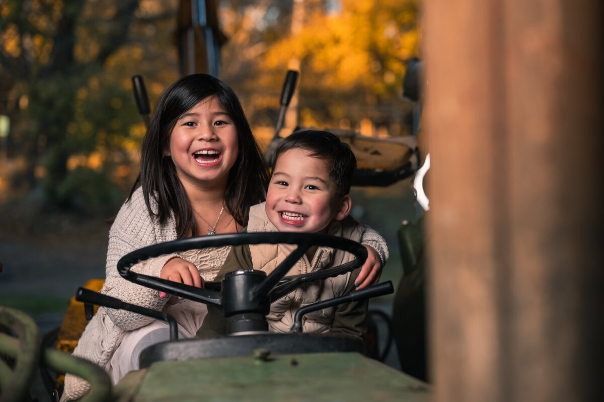 Brother and sister laughing sitting on tractor having a fun family photo session