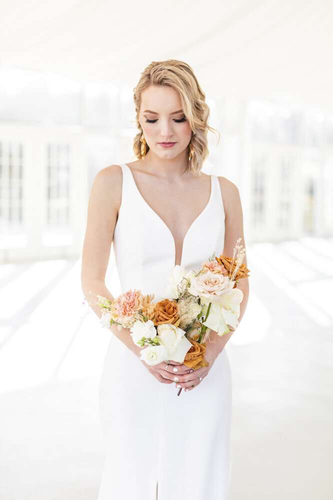 bride in a sleek white gown holding a bouquet of white and orange flowers