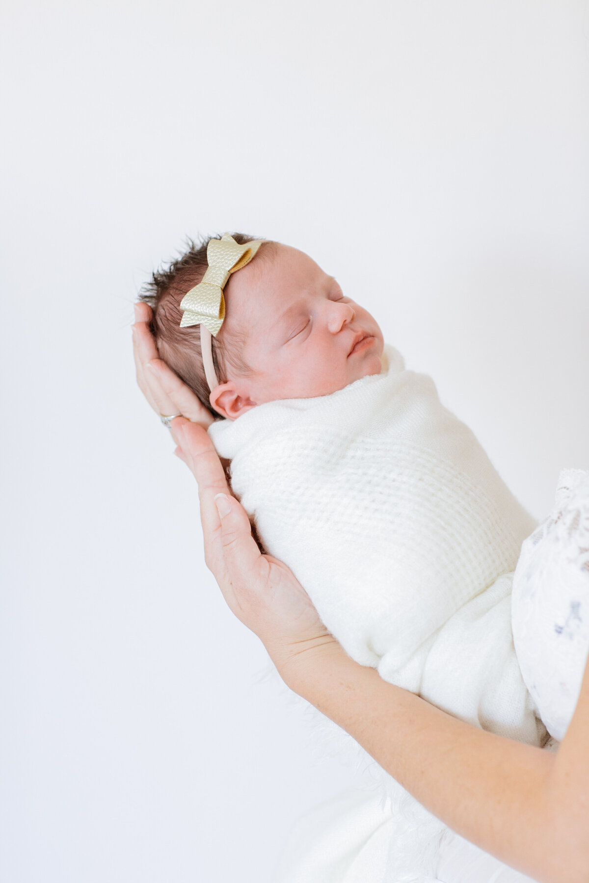 A newborn being held up while swaddled in a white blanket
