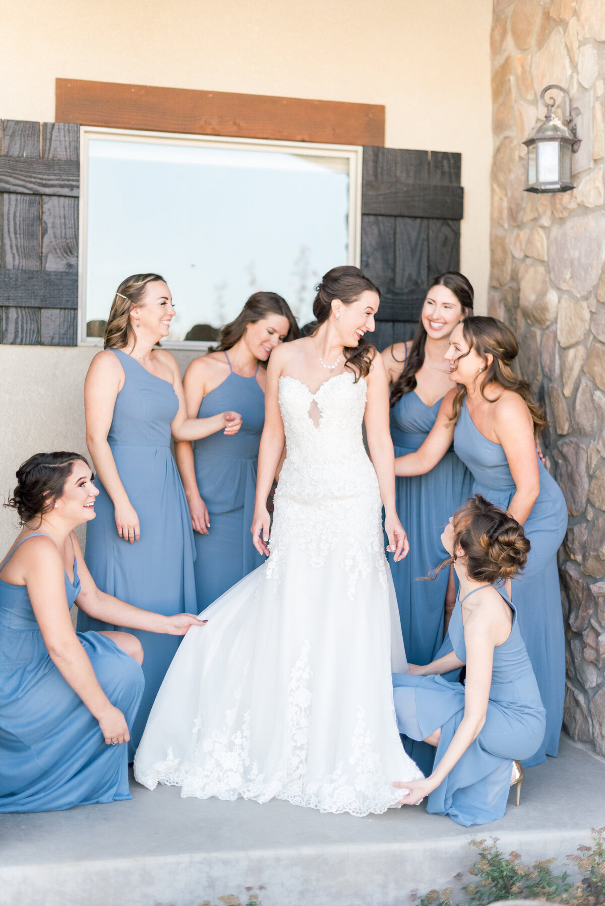 bride getting into her dress witht eh help of her bridesmaids wearing dusty blue
