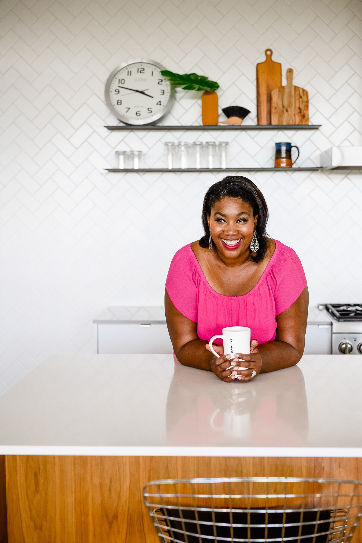 personal branding photos in studio with woman wearing a pink shirt and leaning on a white counter and smiling as she holds a coffee mug photographed by Denver commercial photographers