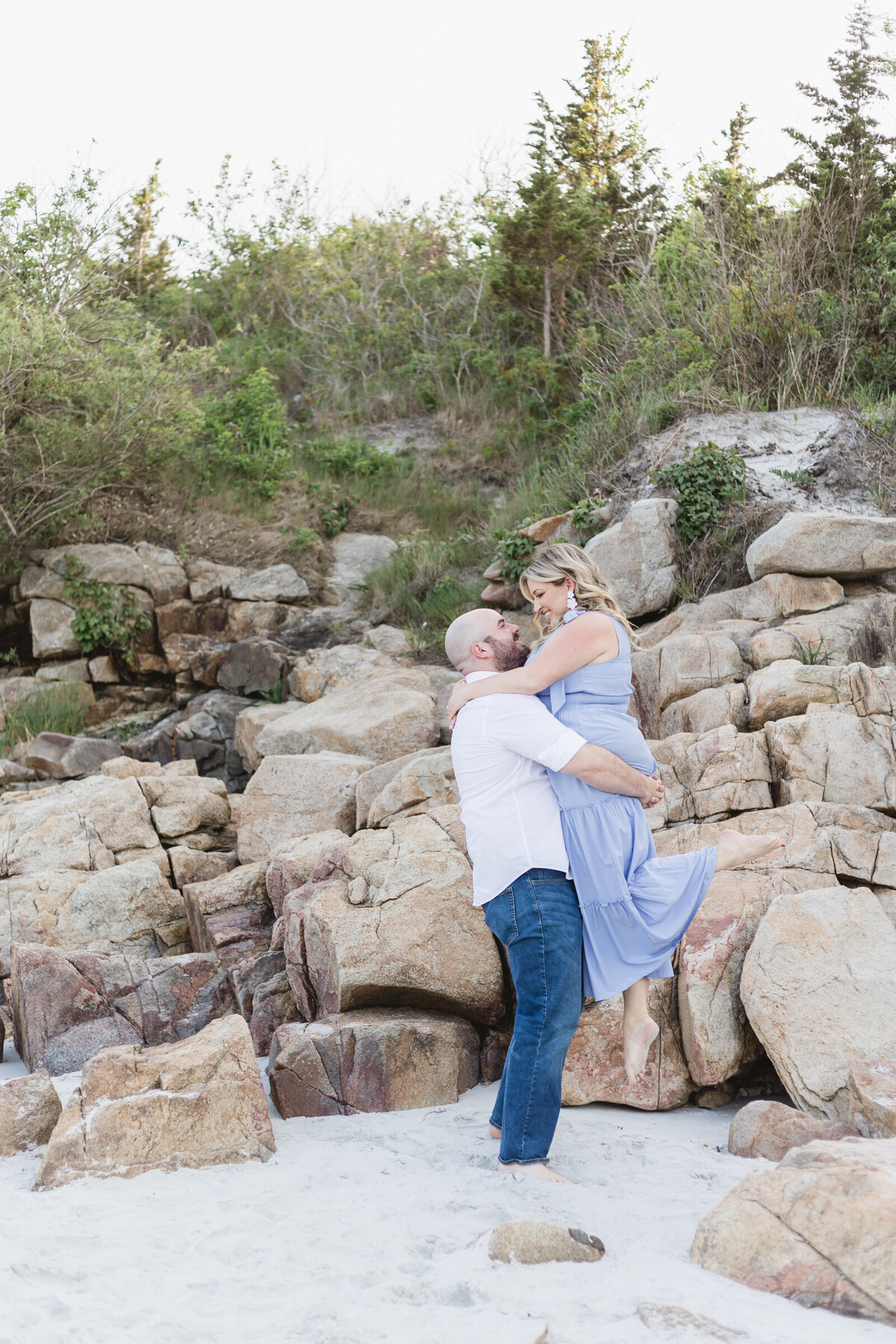 couple lifts his Fiancee during their engagement shoot on a North Shore beach