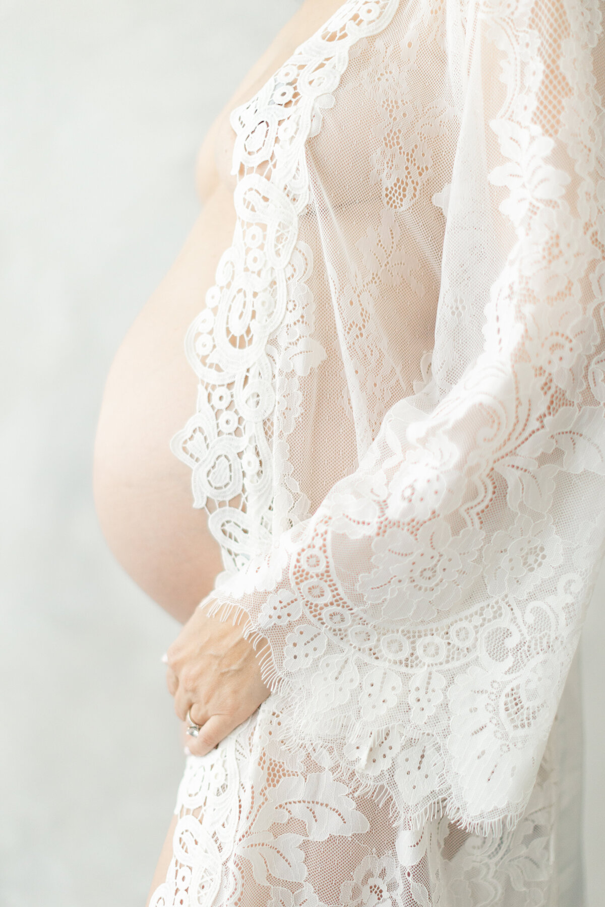 Pregnant woman poses in lacey robe for maternity portraits
