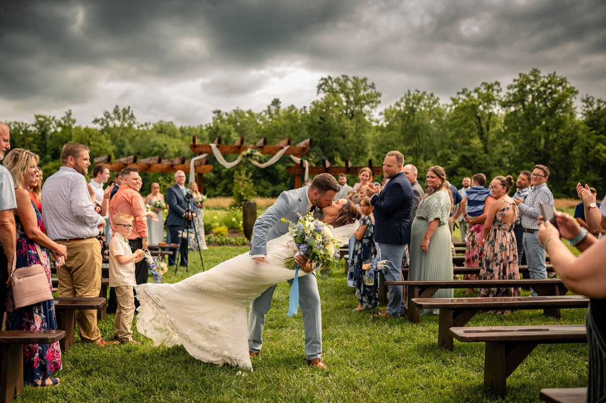 Groom dips bride for a kiss in front of the pergola as guests cheer