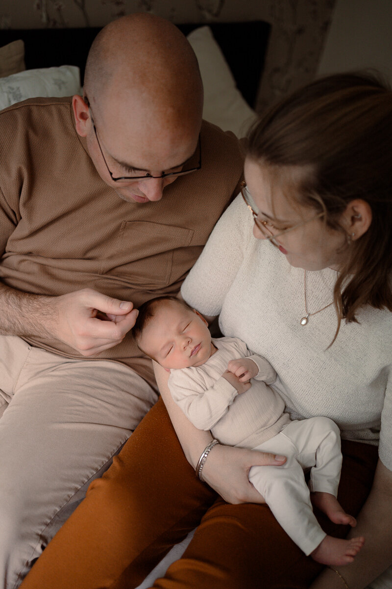 Moeder heeft pasgeboren baby op haar arm en vader aait de baby over zijn haartjes