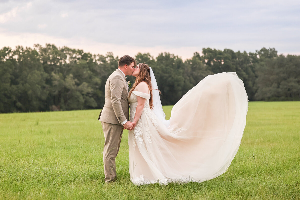 bride and groom kissing in field holding hands at camp retreat  florida