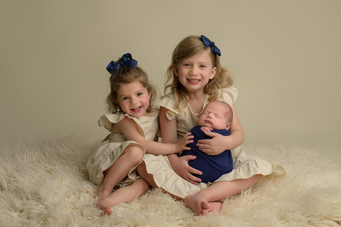 two little girls holding their newborn baby brother