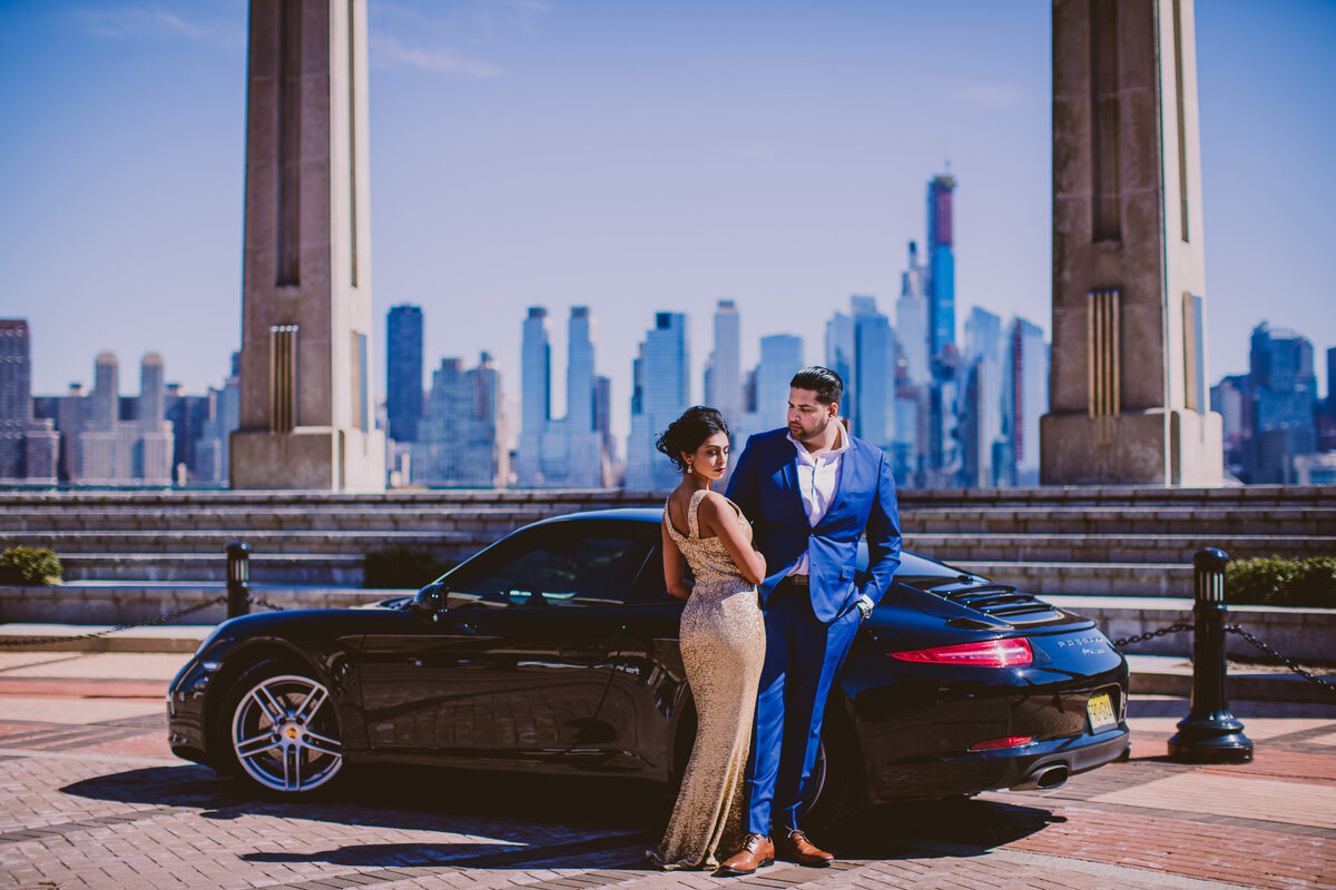 A couple standing near a porsche at the riverwalk nj with the skyline view of nyc