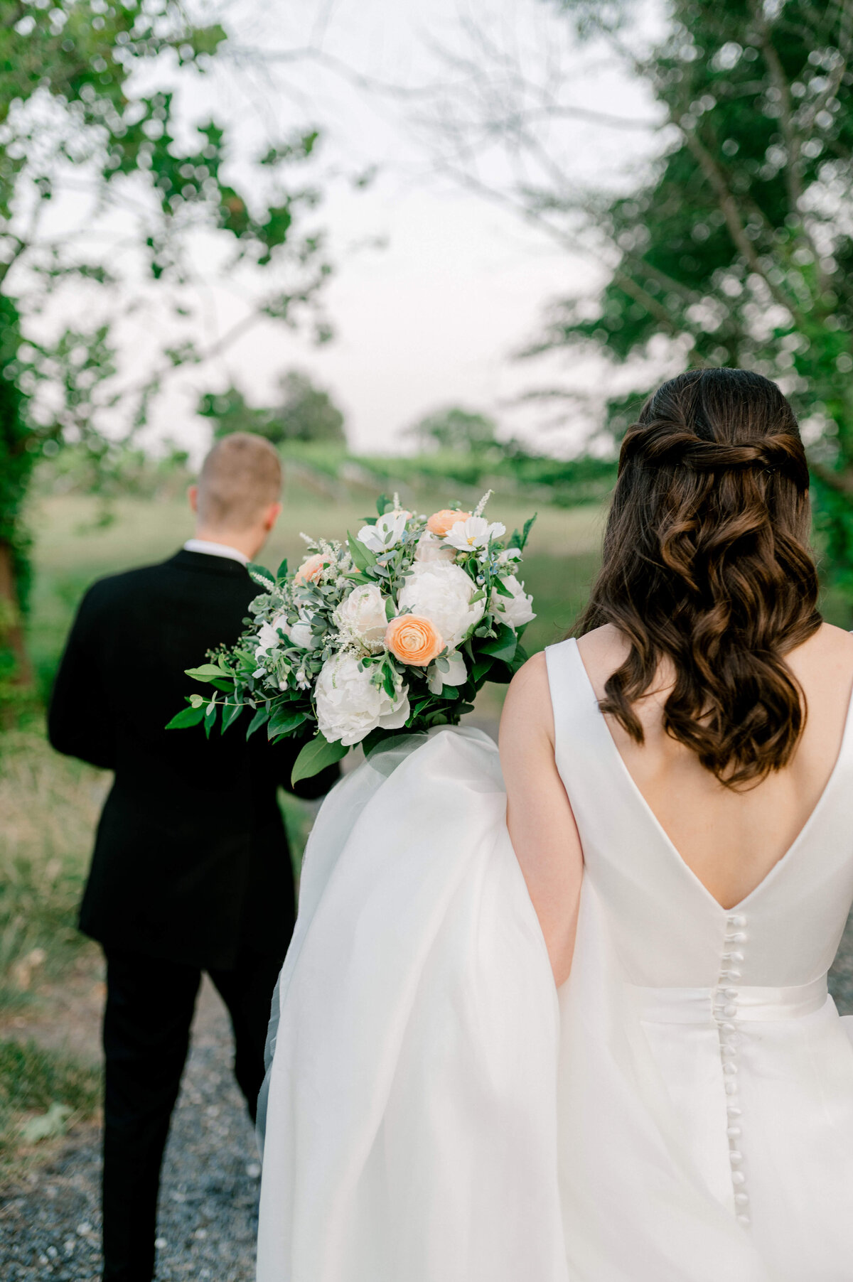 Bride walking towards dreamy Northern Virginia  Winery with peach and white bridal bouquet in hand.