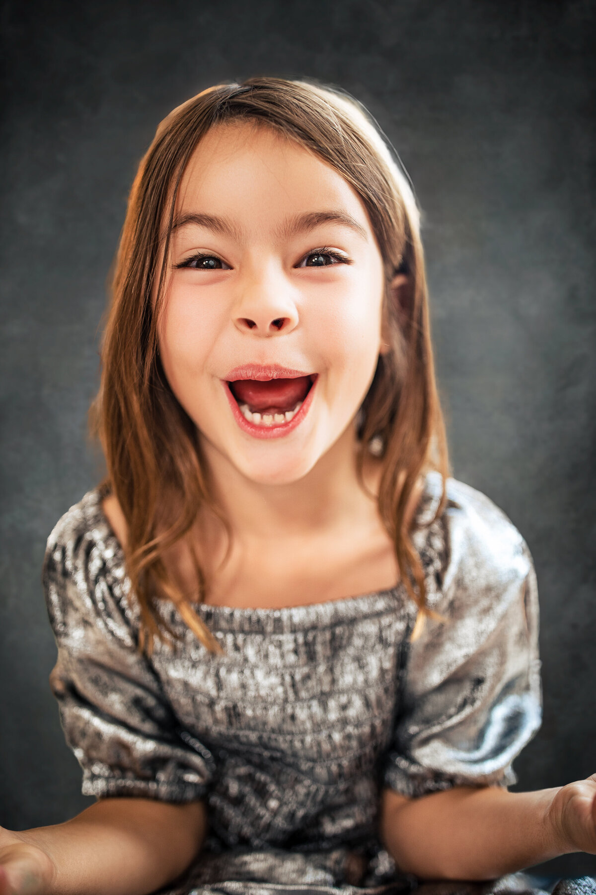 A girl makes a silly face with a sparkly smile and a laugh during the children's mini session with larger than life photography