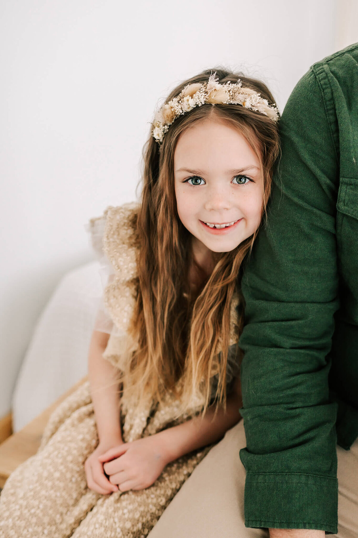 girl in floral crown leaning on dad shoulder in family photo studio in Springfield MO