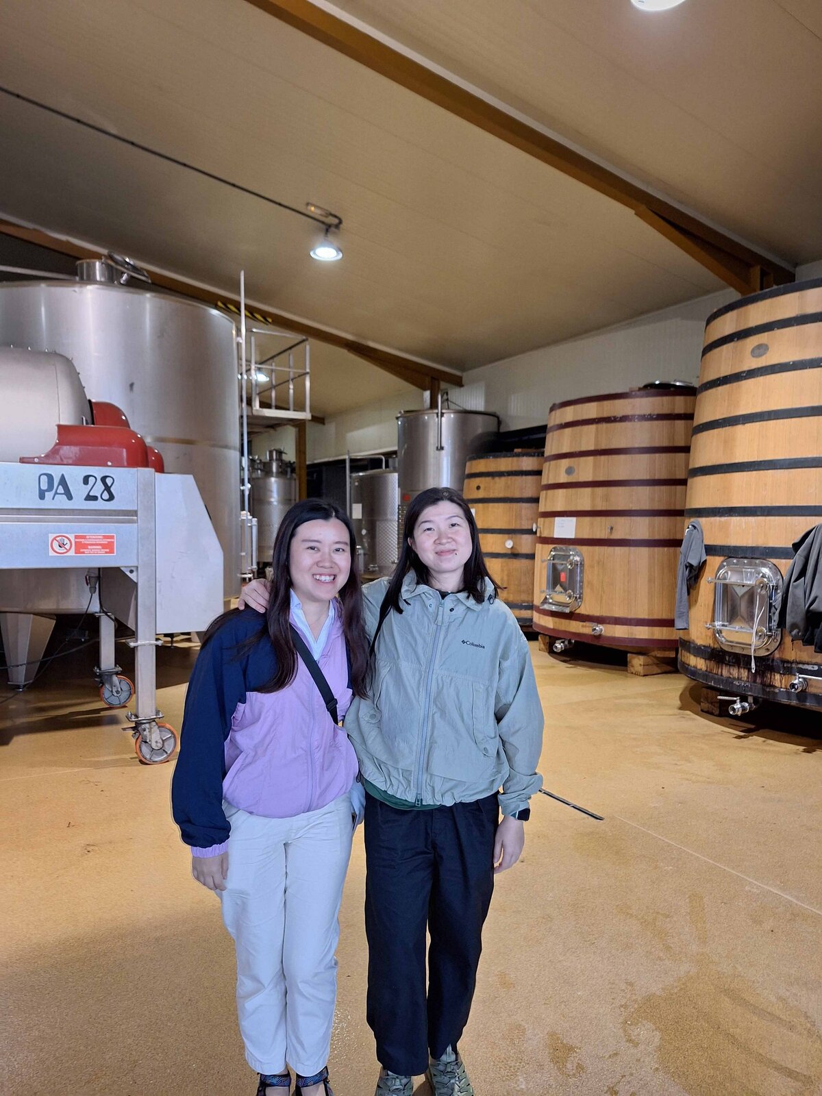 Two women standing near the large vats of wine while learning about the winery's unique wine making process.