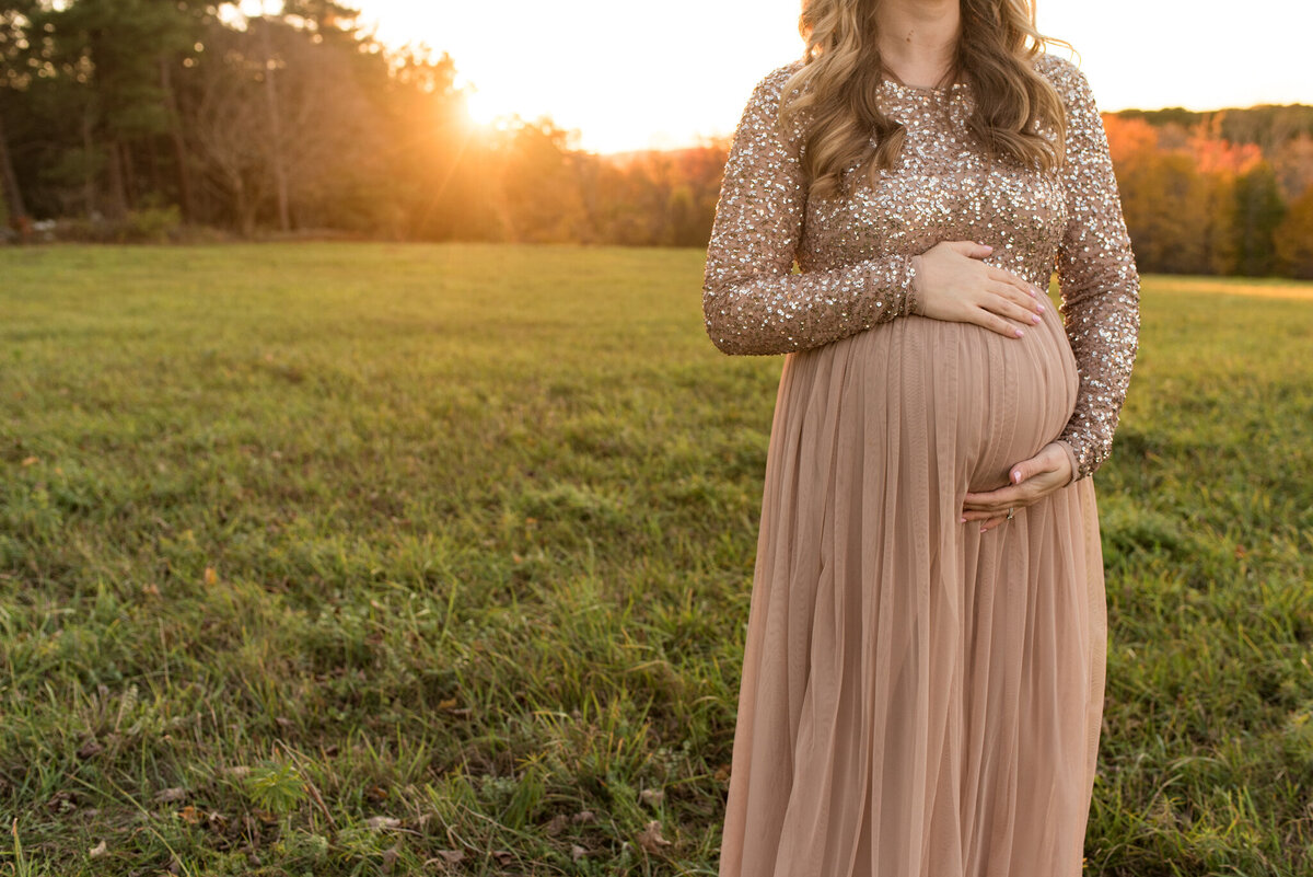 Pregnant mother standing in field at sunset, just her pregnant stomach is in the frame
