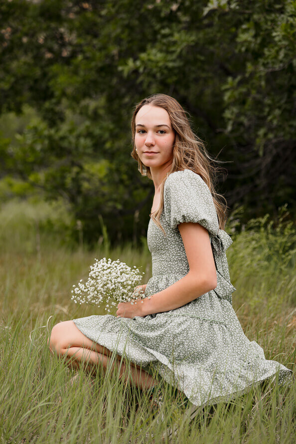 Girl squats and hols baby's breath in a grassy field.