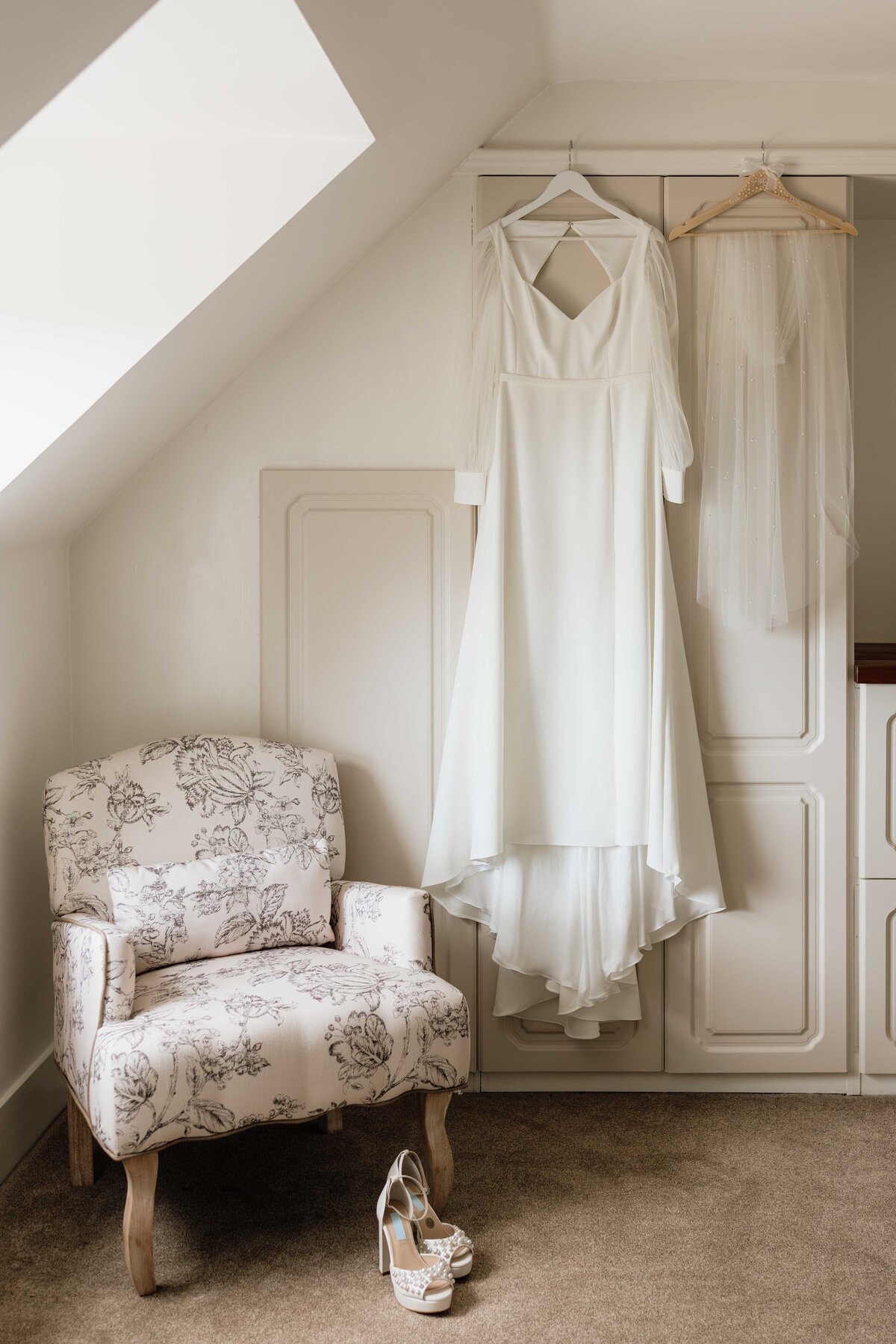 A dress is photographed hanging in a bedroom. The light is moody.