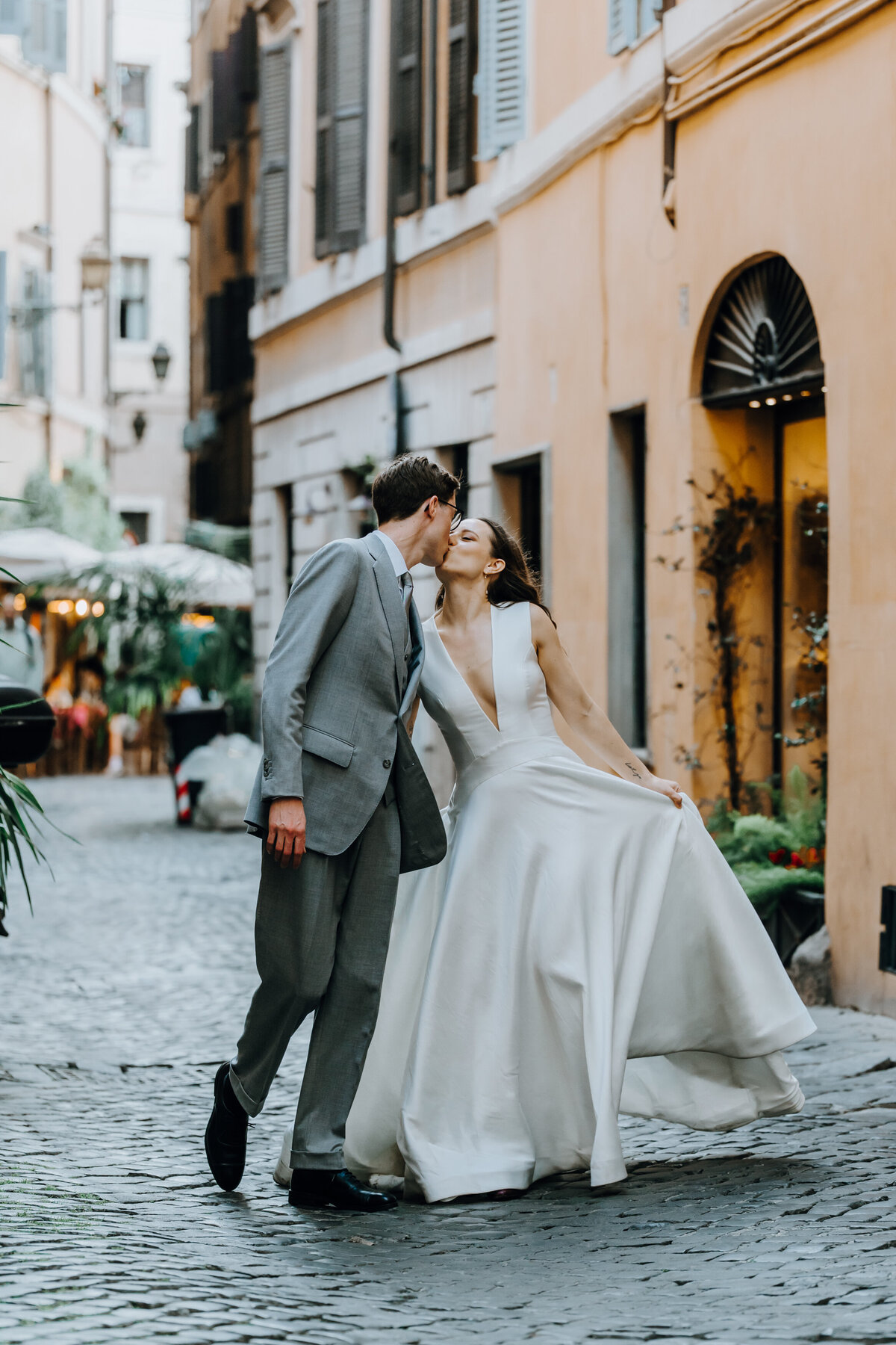 Groom kissing bride’s cheek on cobblestone street.