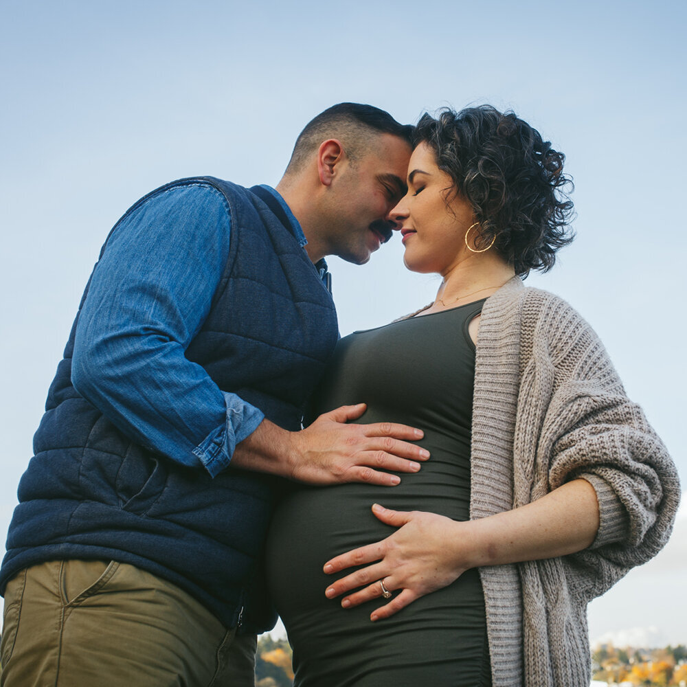 A couple posing with their hands on  the woman's pregnant belly during a maternity session.