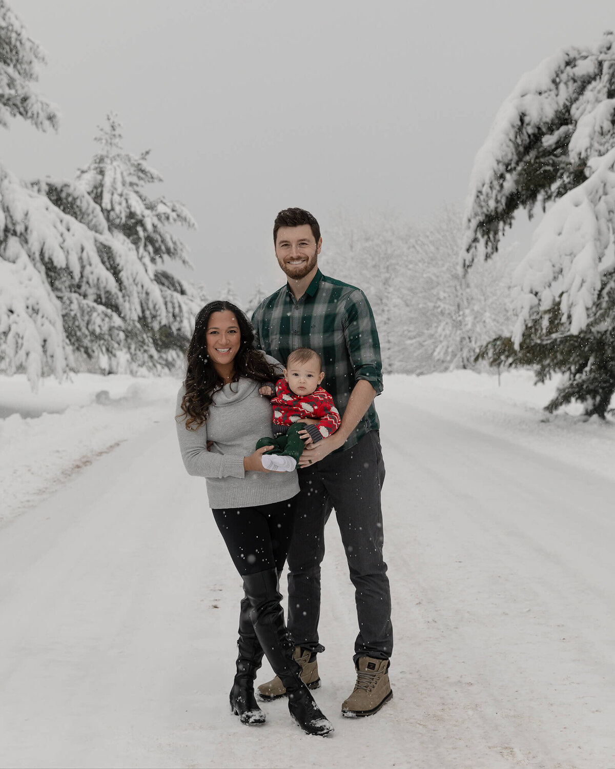 Mom, Dad and little boy standing outside on a beautiful snowy day with lots of heavy snow sitting on the trees.