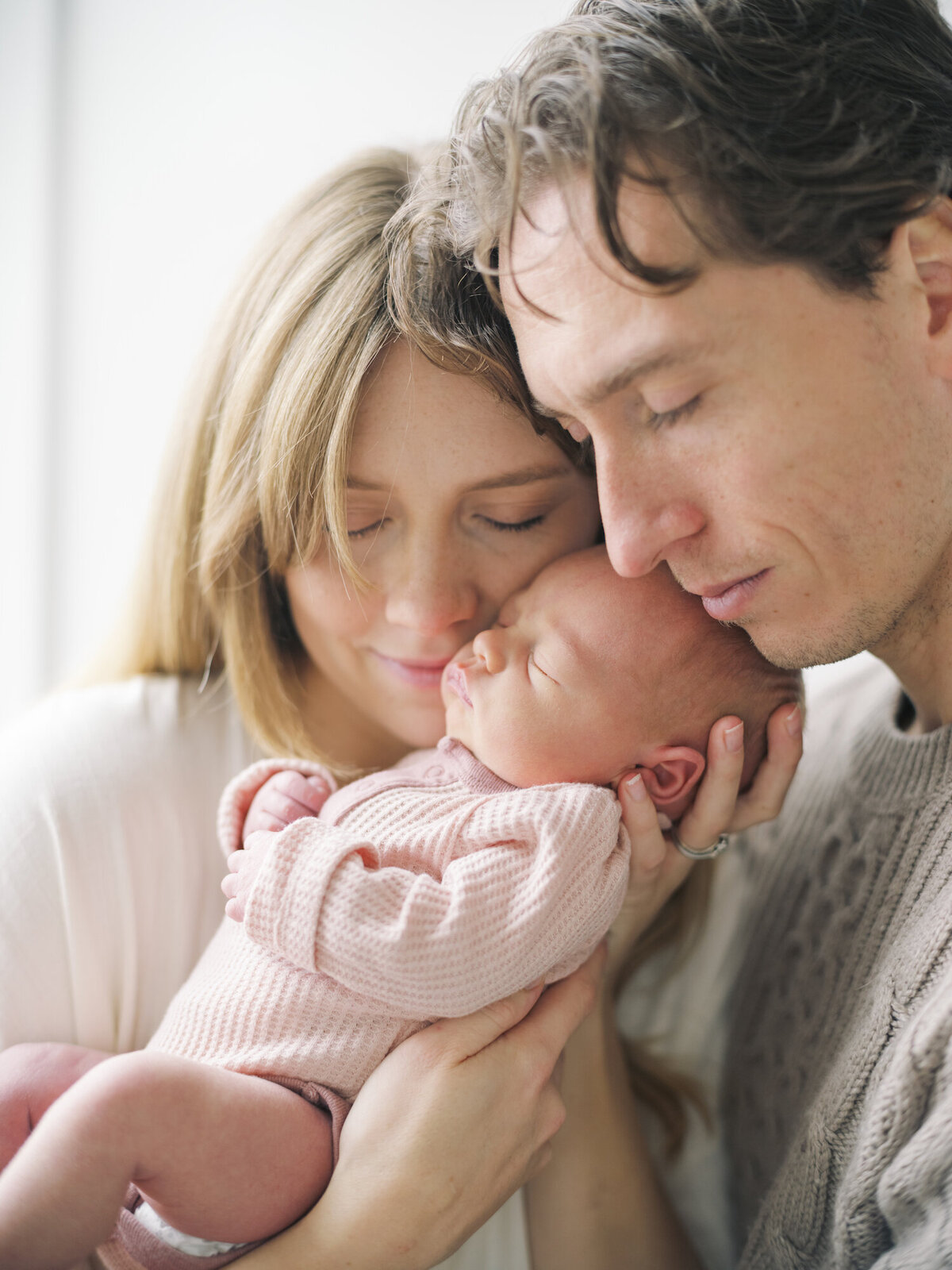 Seattle Newborn Photos of baby girl in pink onsie up close to mom and dads face 