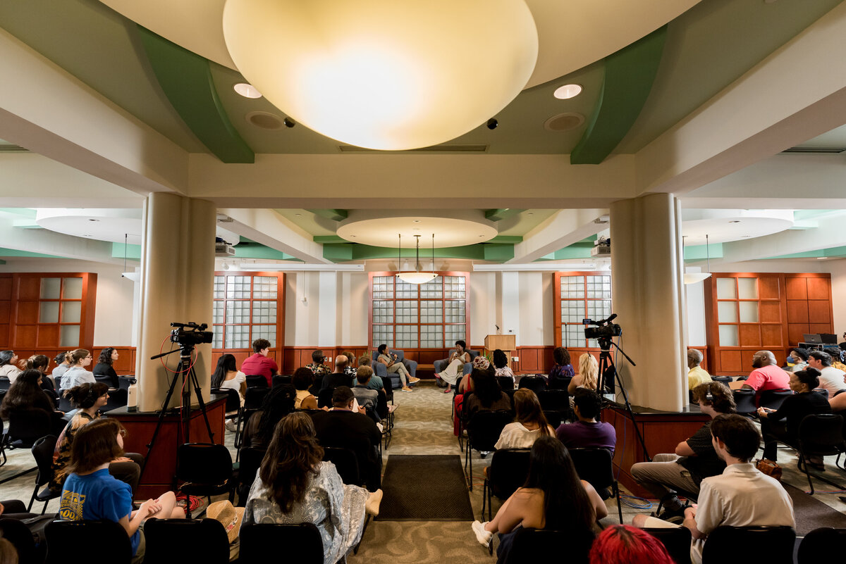 an image photographed from the back of the room, focusing on a crowd and two presenters