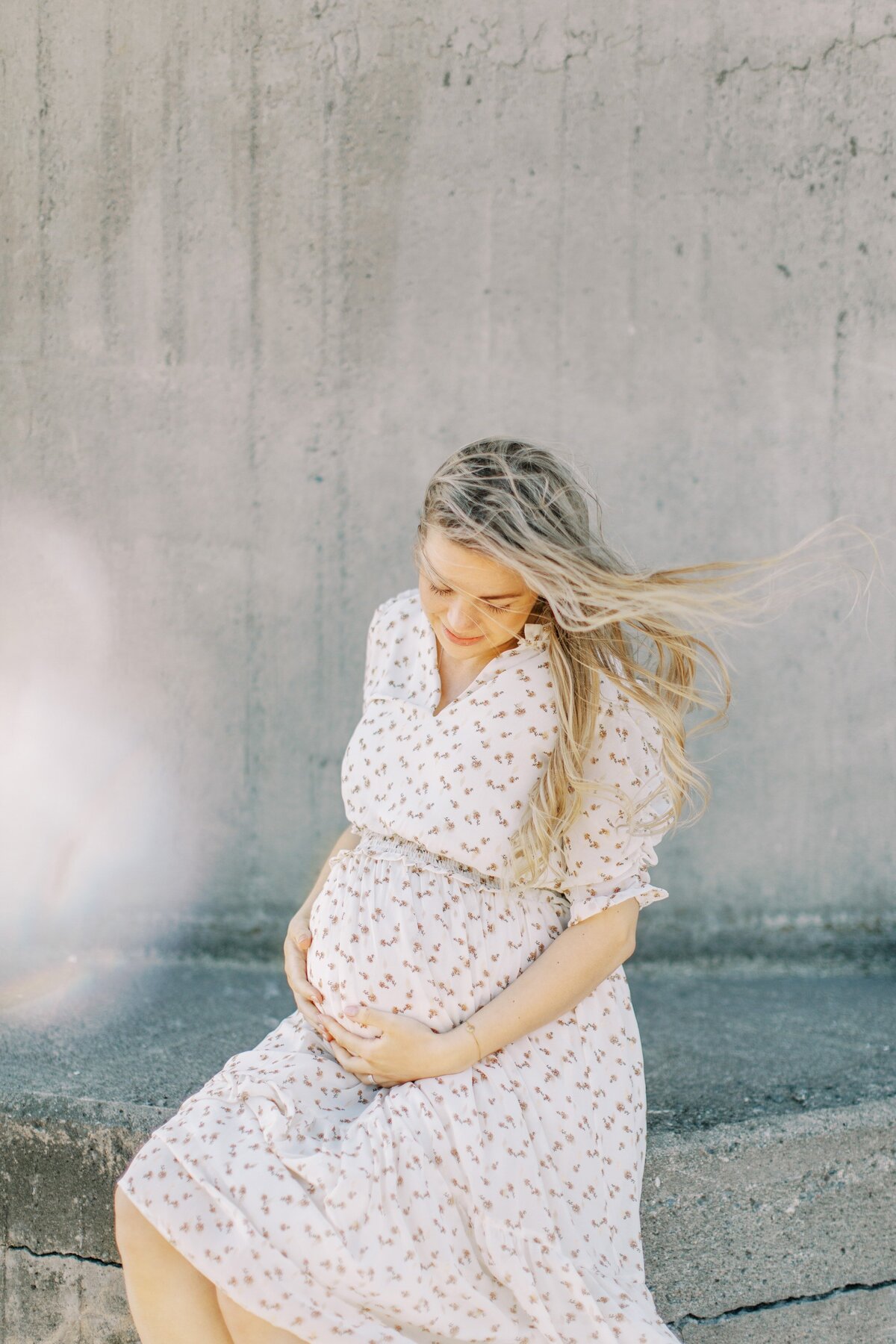 Gravid i blommig klänning sitter och håller om magen i Västerås