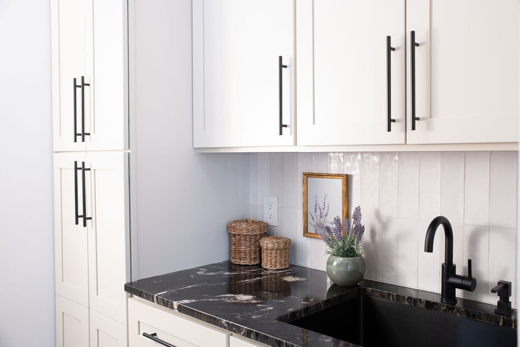 a laundry room with black counters, a black sink, and off-white cabinets