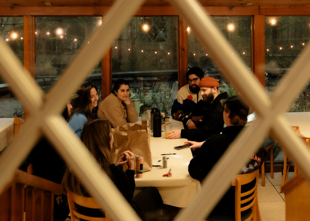 Family and friends laugh around a table in a cozy vacation rental having breakfast before a micro wedding day in Washington.