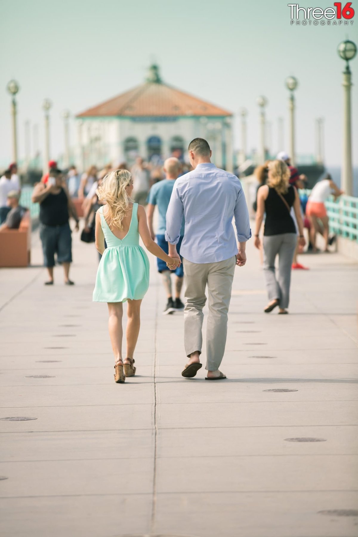 Engaged couple walk down the Manhattan Beach Pier holding hands