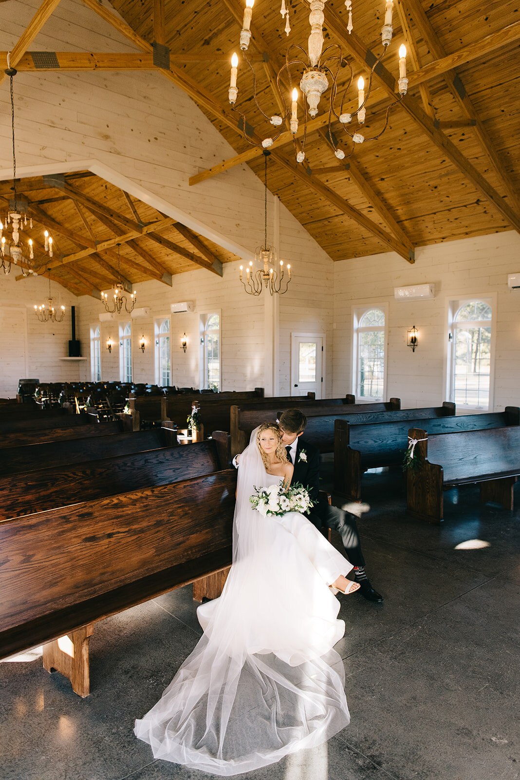 Bride and groom sitting in pews with white and green floral bouquet designed by Abby Grace Florals at Saluda SC wedding