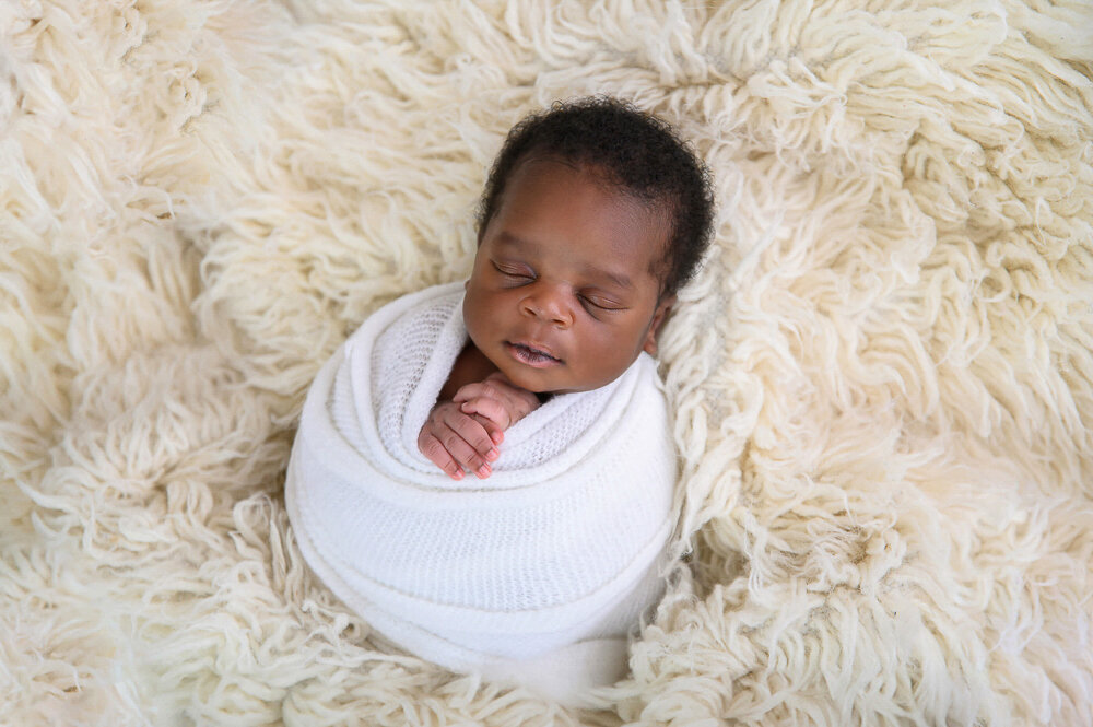 black newborn baby boy wrapped in white on a cream rug for her Hamilton, Ontario newborn photography session.