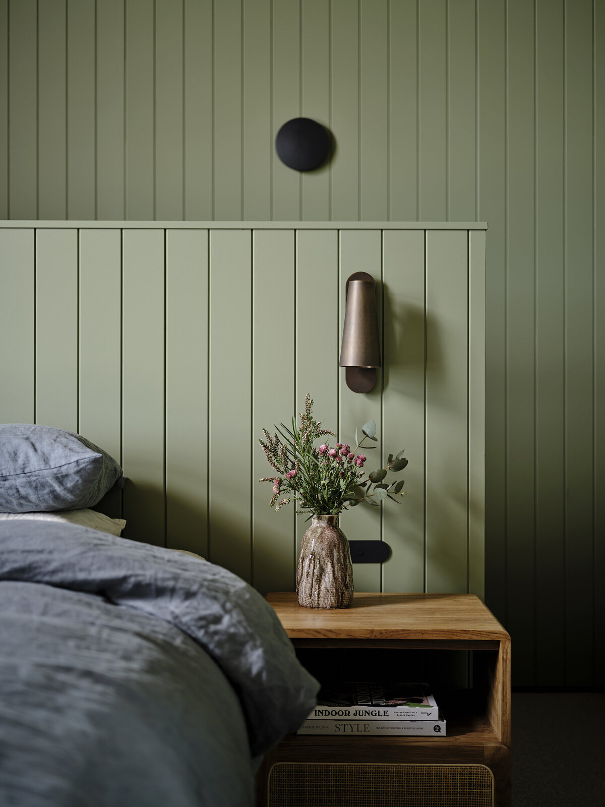 A serene bedroom with sage green VJ panelled wall, timber bedside table, and linen bedding styled by interior designer Melbourne in Strathcreek.