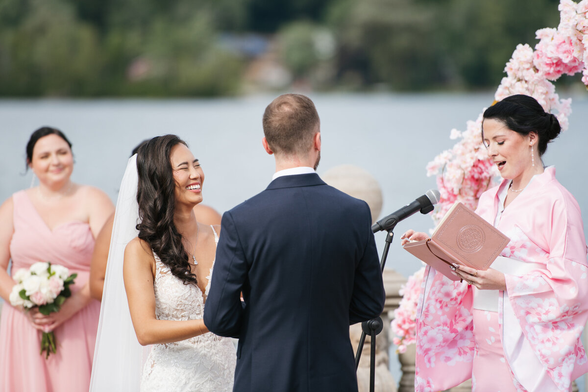 A romantic waterfront wedding at Grand View in Mendon, MA, featuring a joyful couple exchanging vows with a scenic lake backdrop and elegant outdoor decor.
