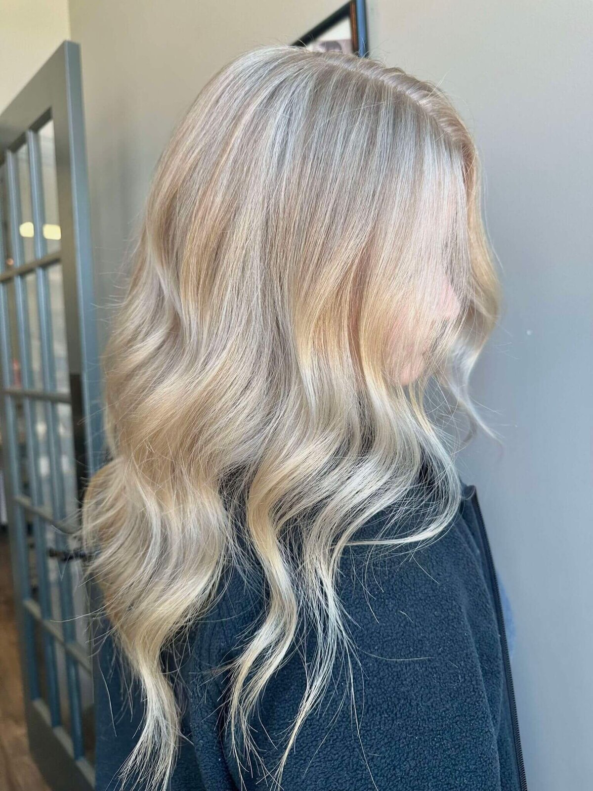 A  woman with long, wavy platinum blonde hair, showcasing a stunning hairstyle created by 212 Salon, Spa, & Barbershop.