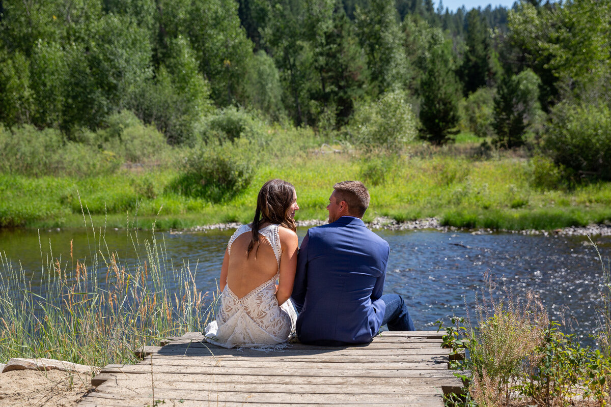 A bride and groom sit on a wooden deck together after their wedding ceremony in Idaho.
